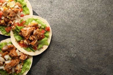 Delicious tacos with vegetables and meat on grey textured table, top view. Space for text