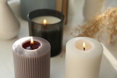 Photo of Different burning candles on white table. Decoration element