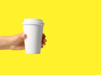 Photo of Woman holding takeaway paper coffee cup on yellow background, closeup. Space for text