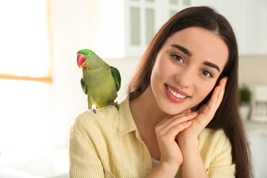 Young woman with Alexandrine parakeet indoors. Cute pet