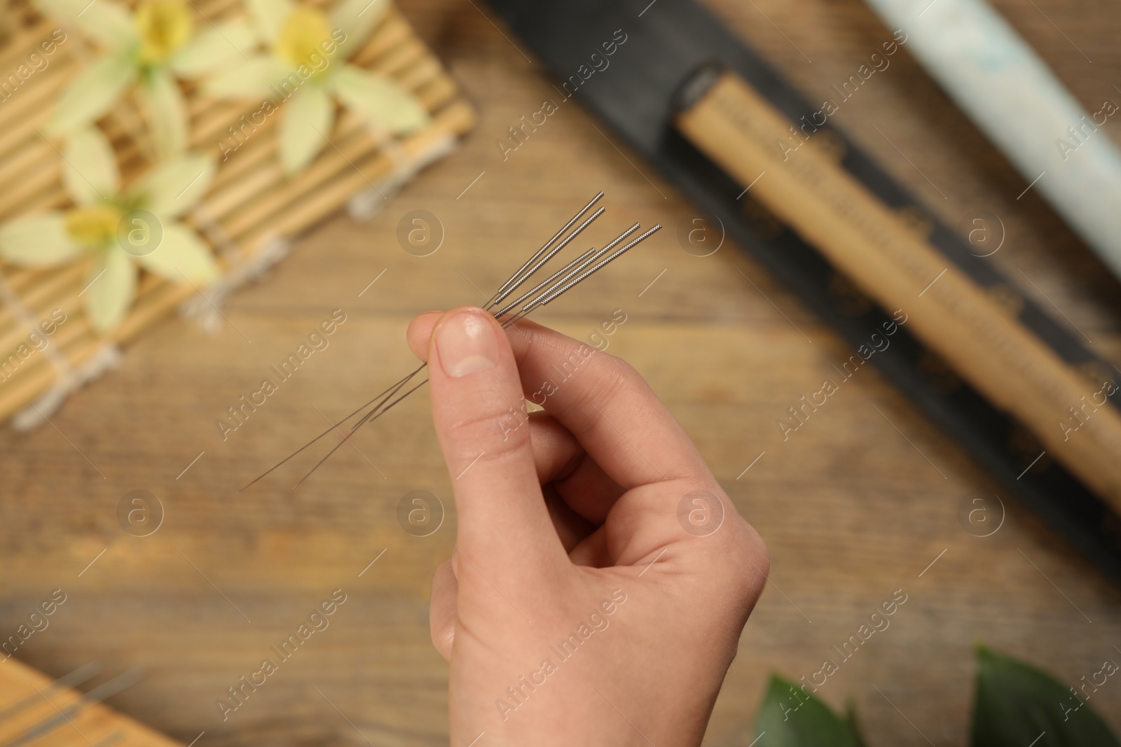 Photo of Woman holding many acupuncture needles over wooden table, closeup