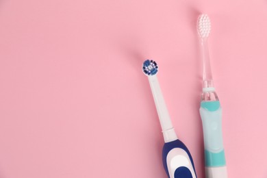 Electric toothbrushes on pink background, flat lay. Space for text