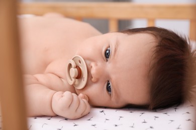 Photo of Cute little baby with pacifier lying in comfortable crib, closeup. Bedtime