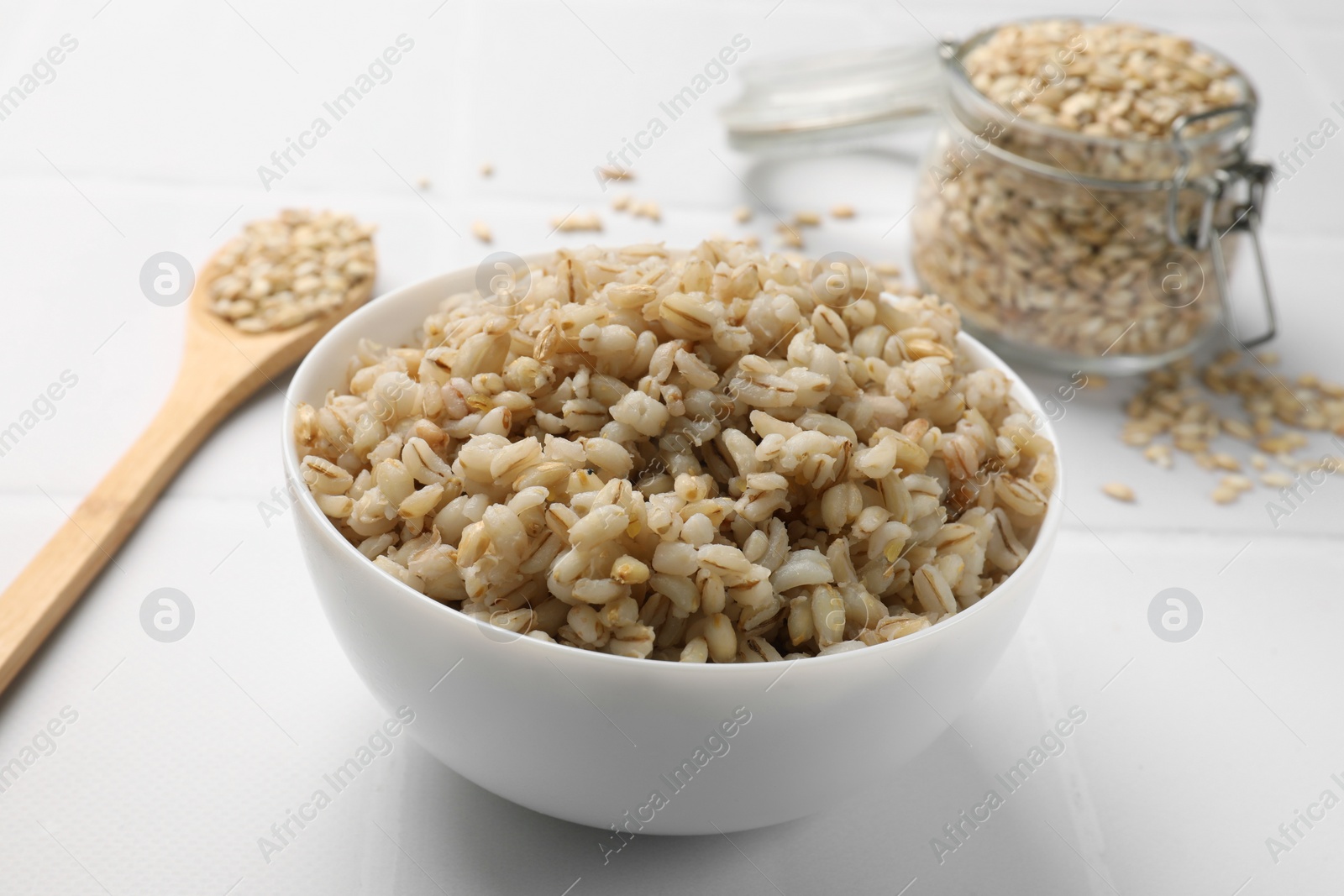 Photo of Delicious pearl barley in bowl served on white tiled table, closeup