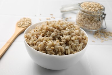 Photo of Delicious pearl barley in bowl served on white tiled table, closeup