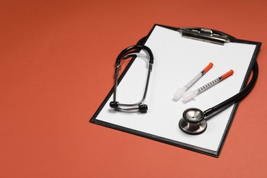 Photo of Stethoscope, syringes and clipboard on crimson background. Space for text