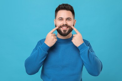 Photo of Happy young man touching mustache on light blue background