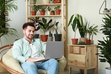 Young man using laptop in room with different home plants