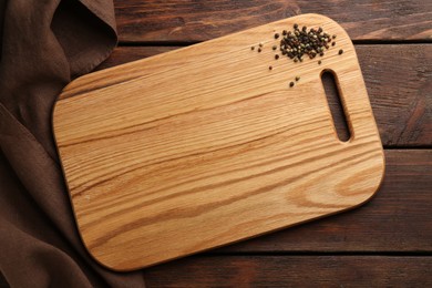 Photo of New cutting board and peppercorns on wooden table, flat lay