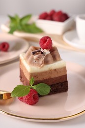 Photo of Piece of triple chocolate mousse cake with raspberries served on table, closeup
