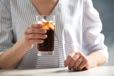 Photo of Woman with glass of cold cola at table on color background, closeup