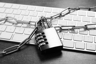 Photo of Cyber security. Metal combination padlock with chain and keyboard on grey table, closeup