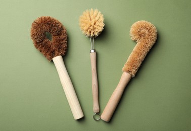 Photo of Different bamboo brushes for dish washing on green background, flat lay. Conscious consumption