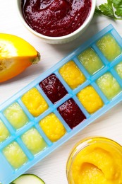 Photo of Different purees in ice cube tray and ingredients on white table, flat lay. Ready for freezing