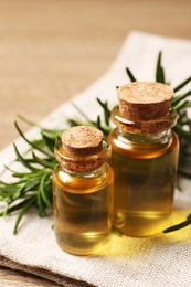 Photo of Bottles with essential oil and fresh rosemary on towel, closeup