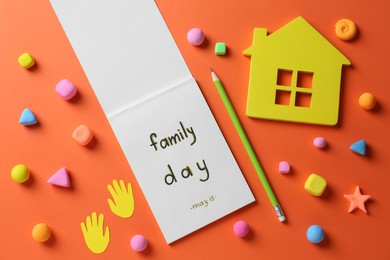 Photo of Happy Family Day. Flat lay composition with notebook and house model on orange background