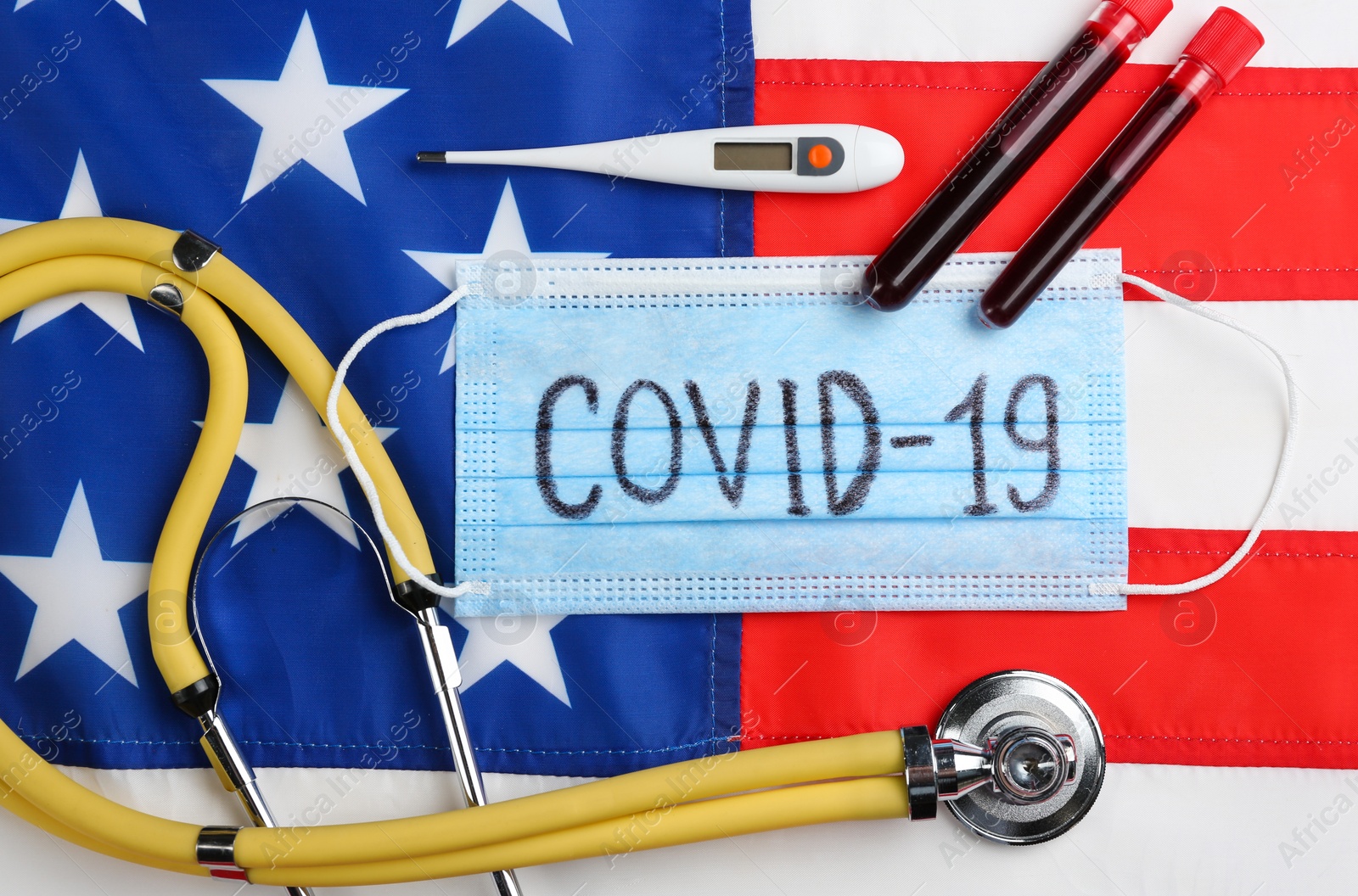 Photo of Test tubes with blood samples, medical mask and stethoscope on American flag, flat lay. Coronavirus pandemic in USA