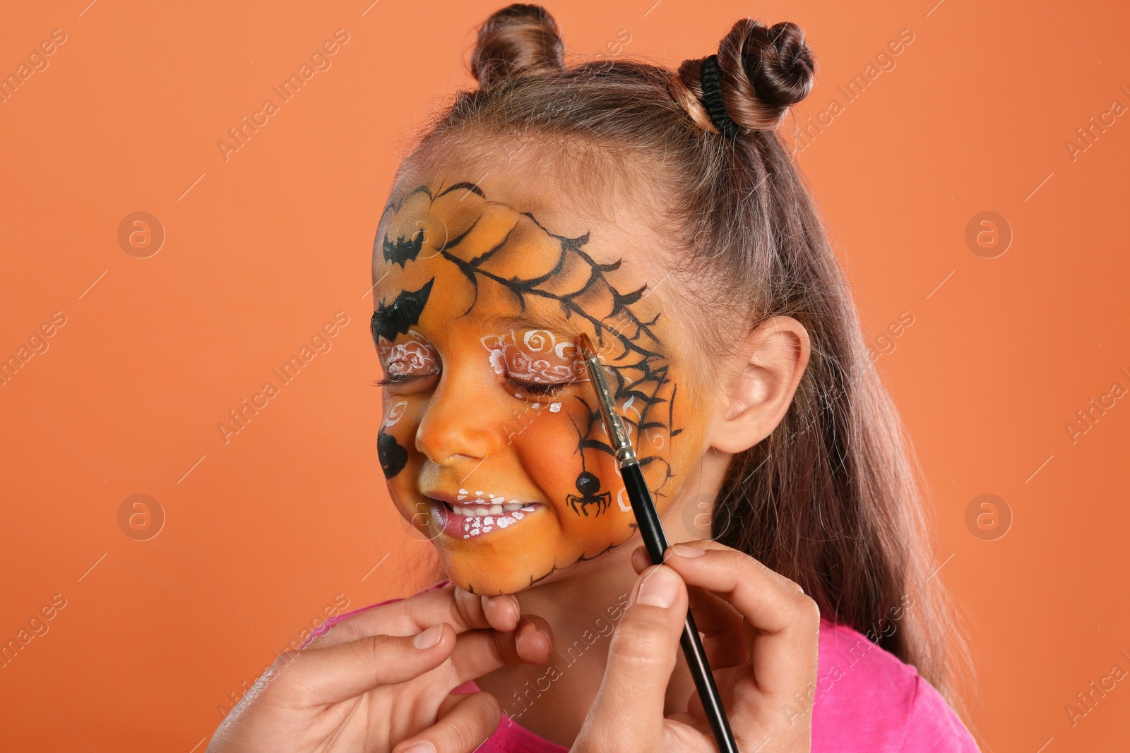 Photo of Artist painting face of little girl on orange background