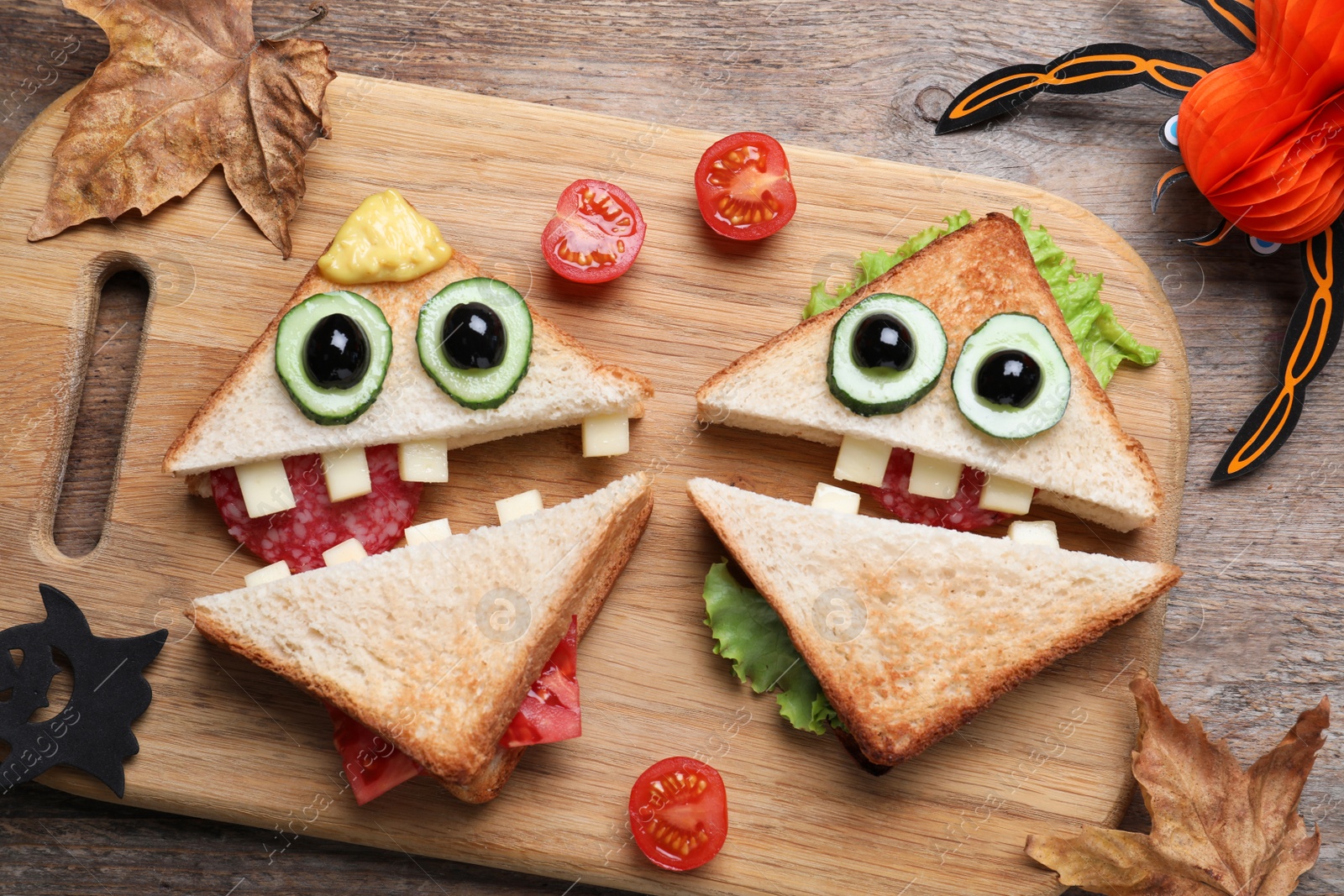 Photo of Cute monster sandwiches served on wooden table, flat lay. Halloween party food