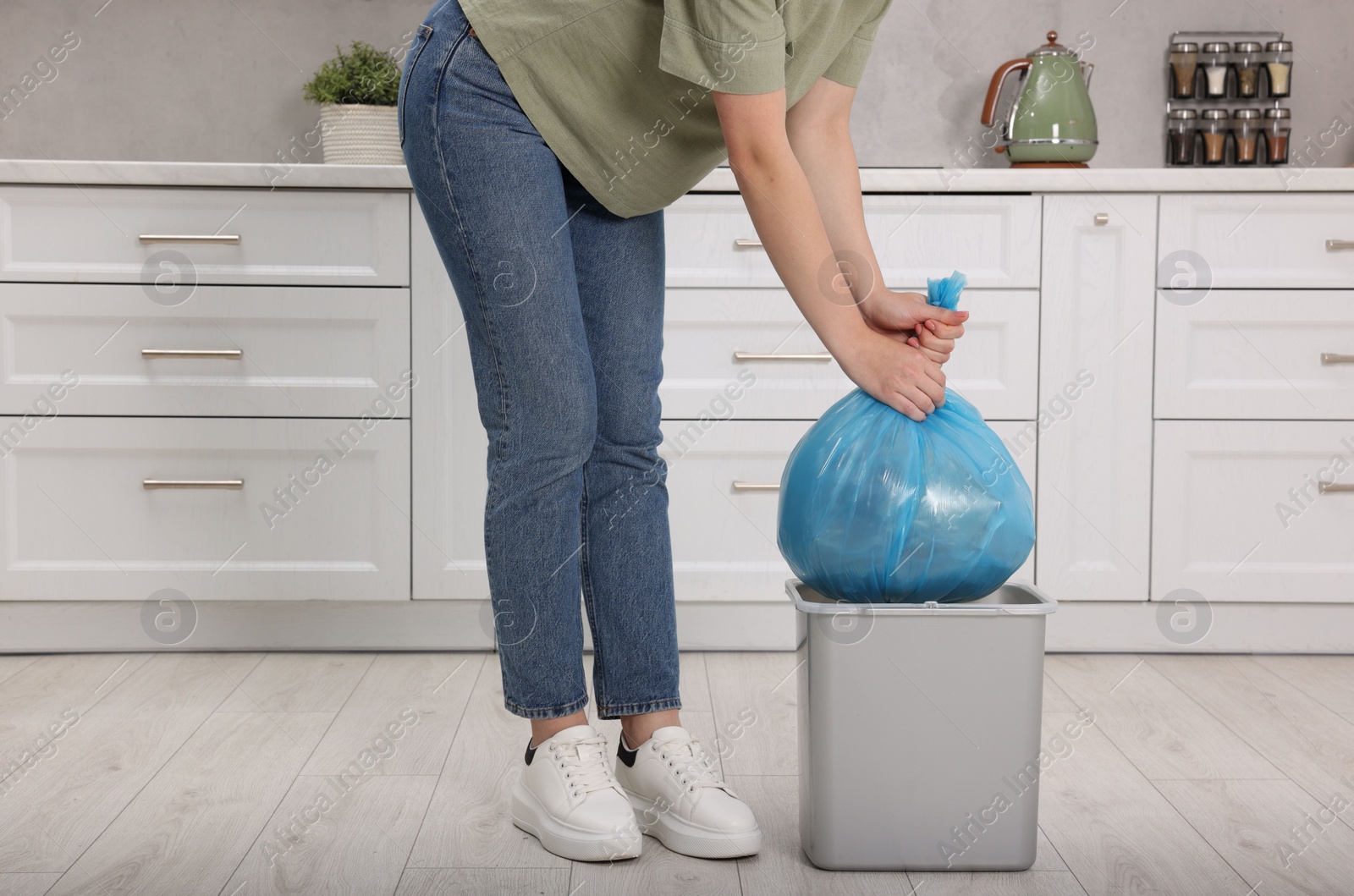 Photo of Woman taking garbage bag out of trash bin in kitchen, closeup