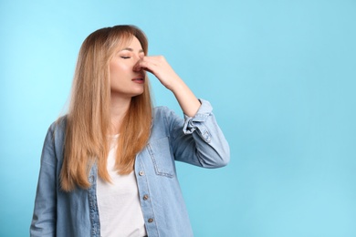 Photo of Young woman suffering from runny nose on light blue background. Space for text