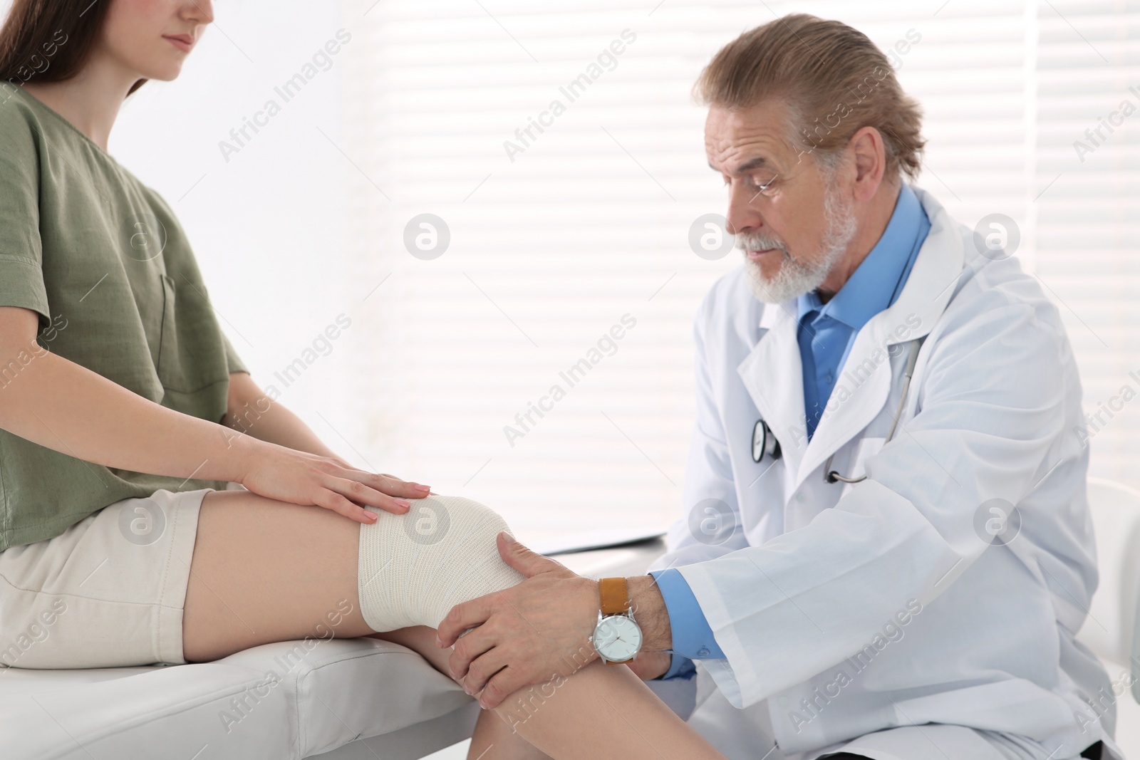 Photo of Orthopedist applying bandage onto patient's knee in clinic