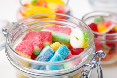 Tasty jelly candies in jars on white table, closeup