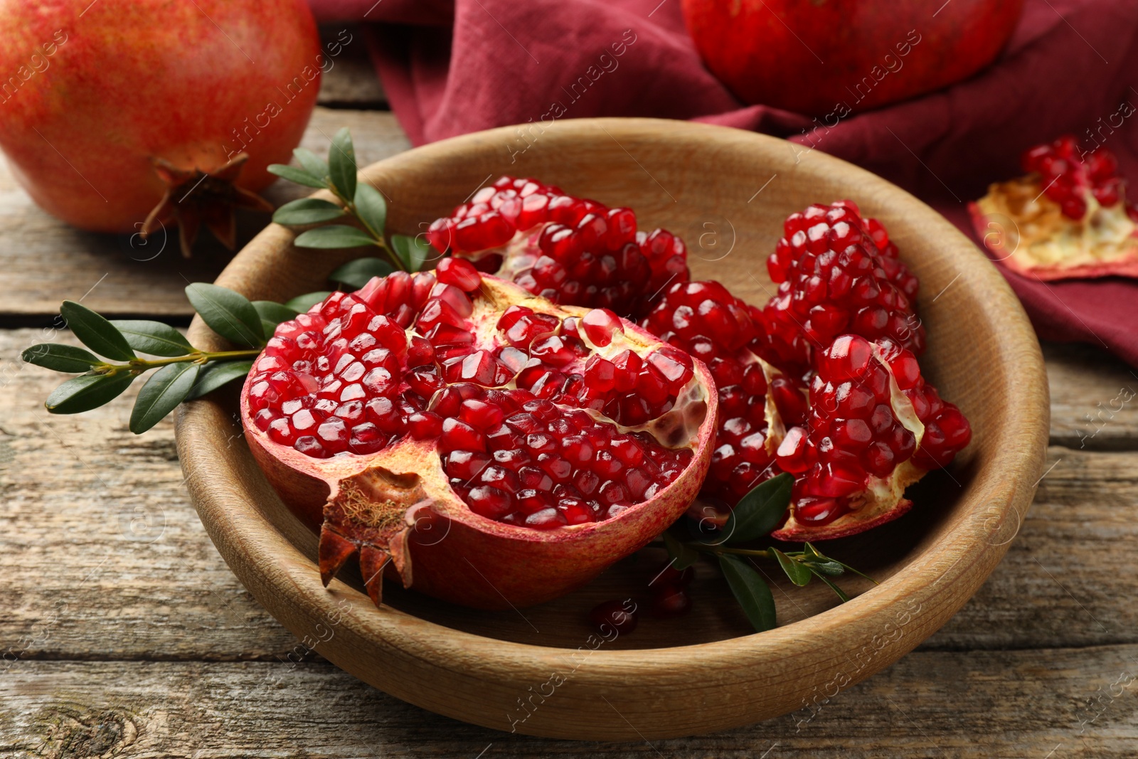 Photo of Fresh pomegranates and green leaves on wooden table, closeup