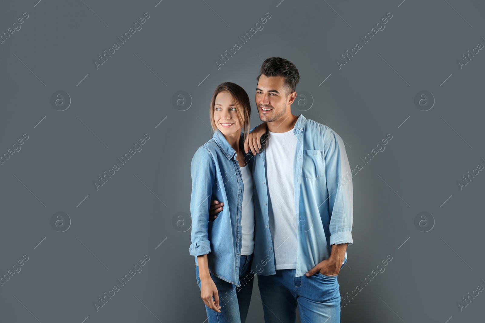 Photo of Young couple in stylish clothes on grey background. T-shirts as mockup for design