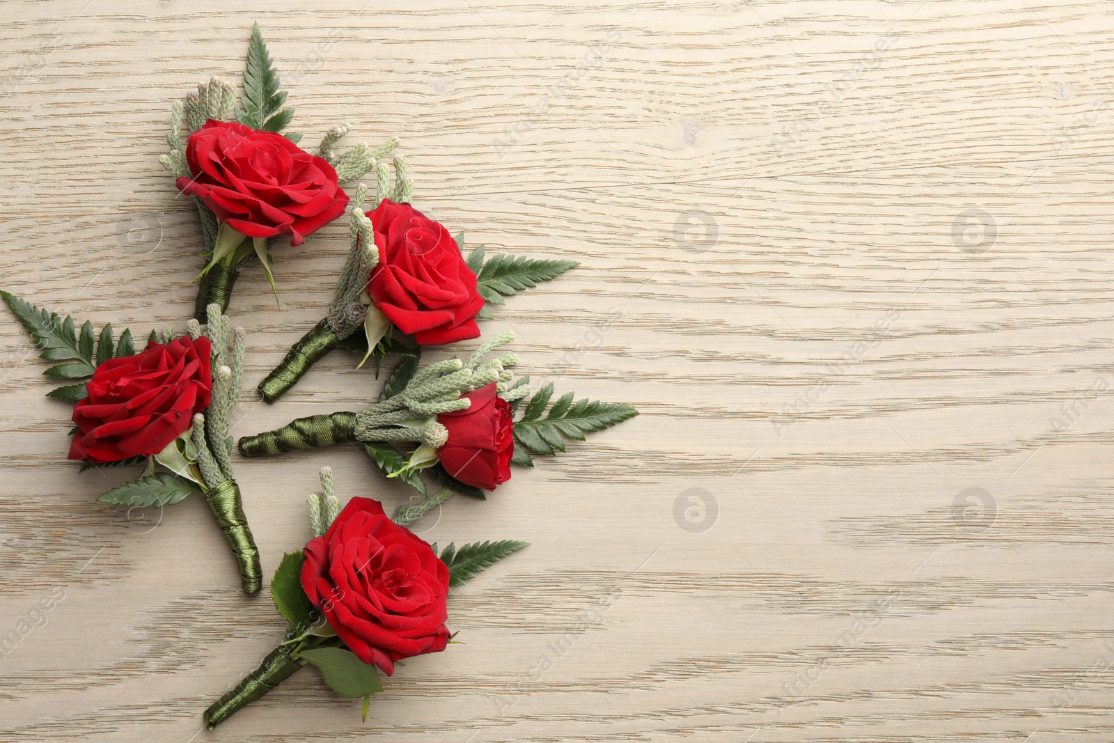 Photo of Many stylish red boutonnieres on light wooden table, flat lay. Space for text