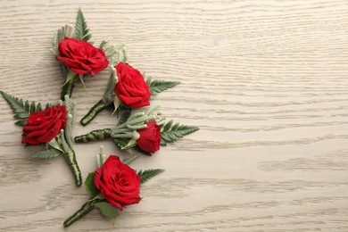 Photo of Many stylish red boutonnieres on light wooden table, flat lay. Space for text