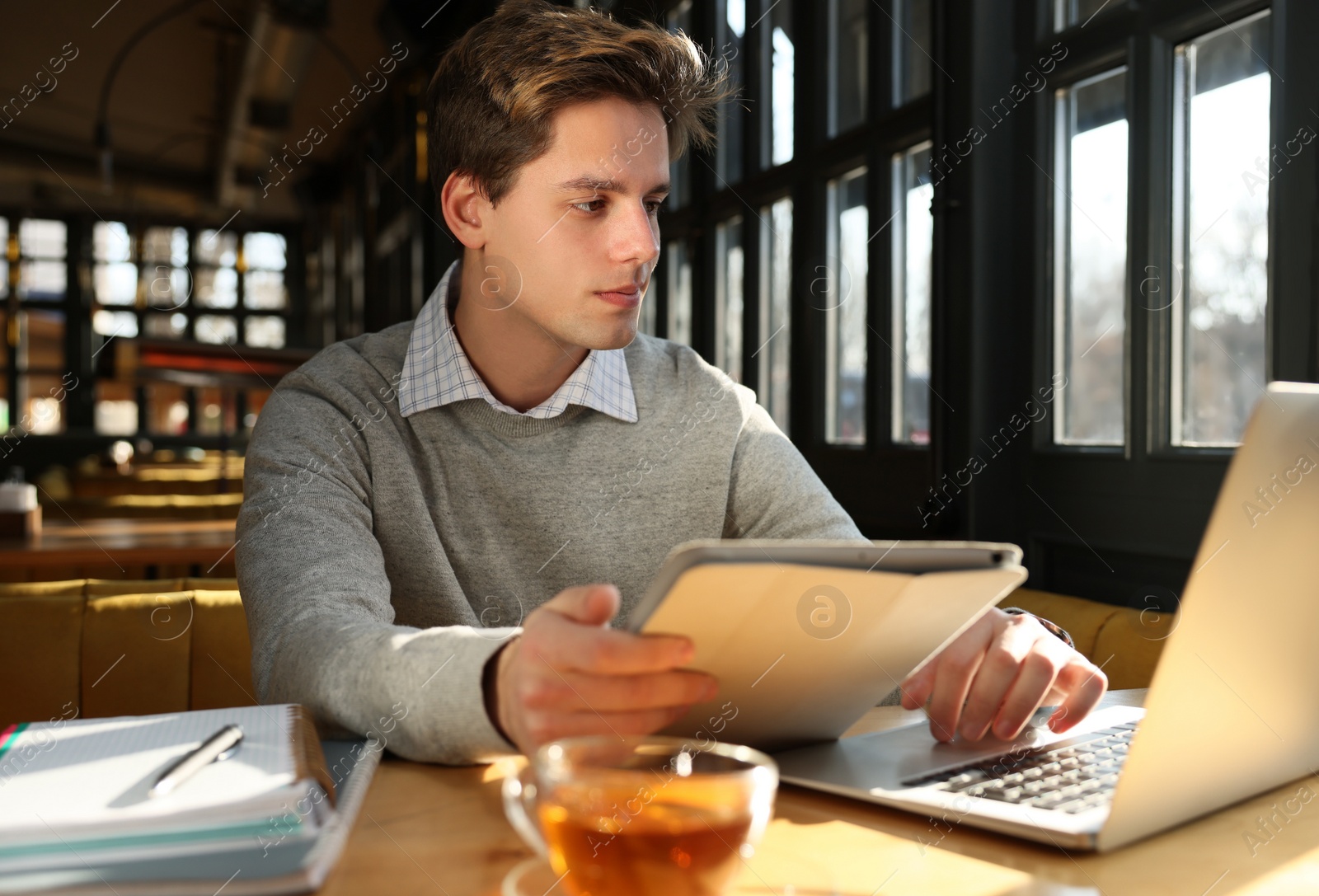 Photo of Teenage student with laptop and tablet studying at table in cafe