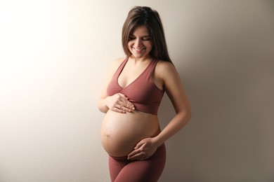 Pregnant young woman touching belly on beige background