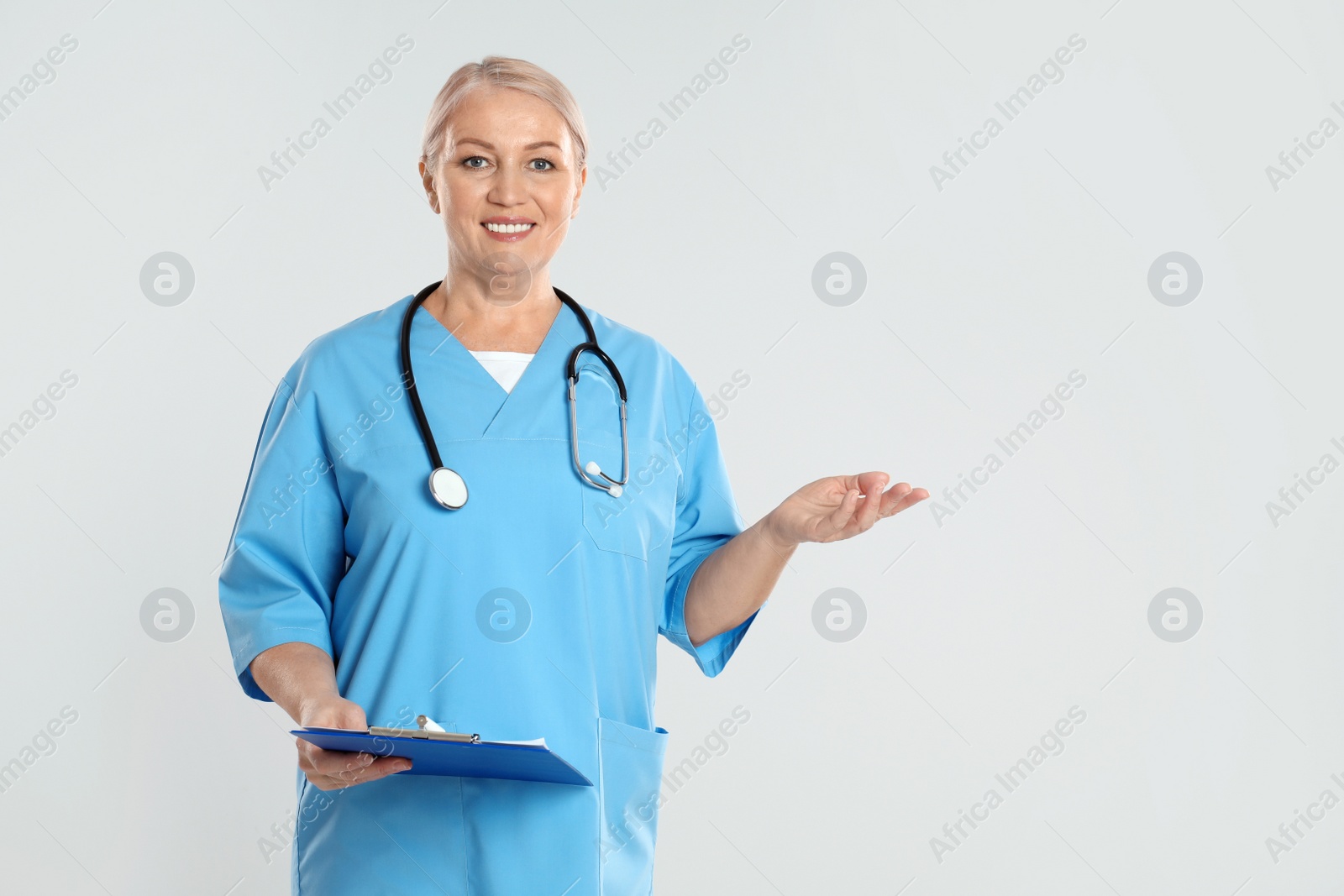 Photo of Mature doctor with clipboard on light grey background. Space for text