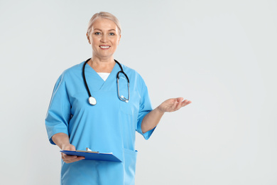 Photo of Mature doctor with clipboard on light grey background. Space for text