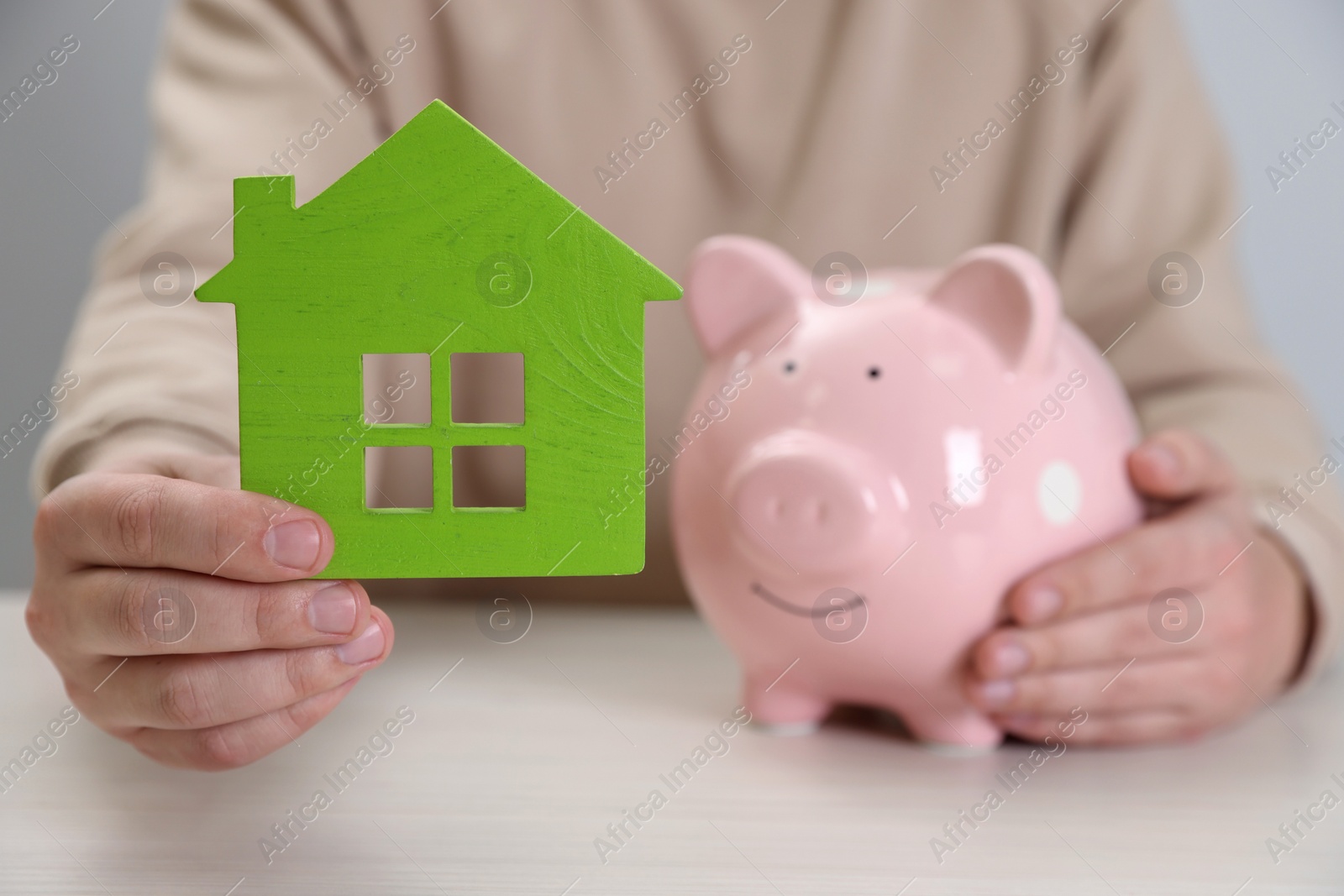 Photo of Man with house model and piggy bank at wooden table, closeup. Saving money concept