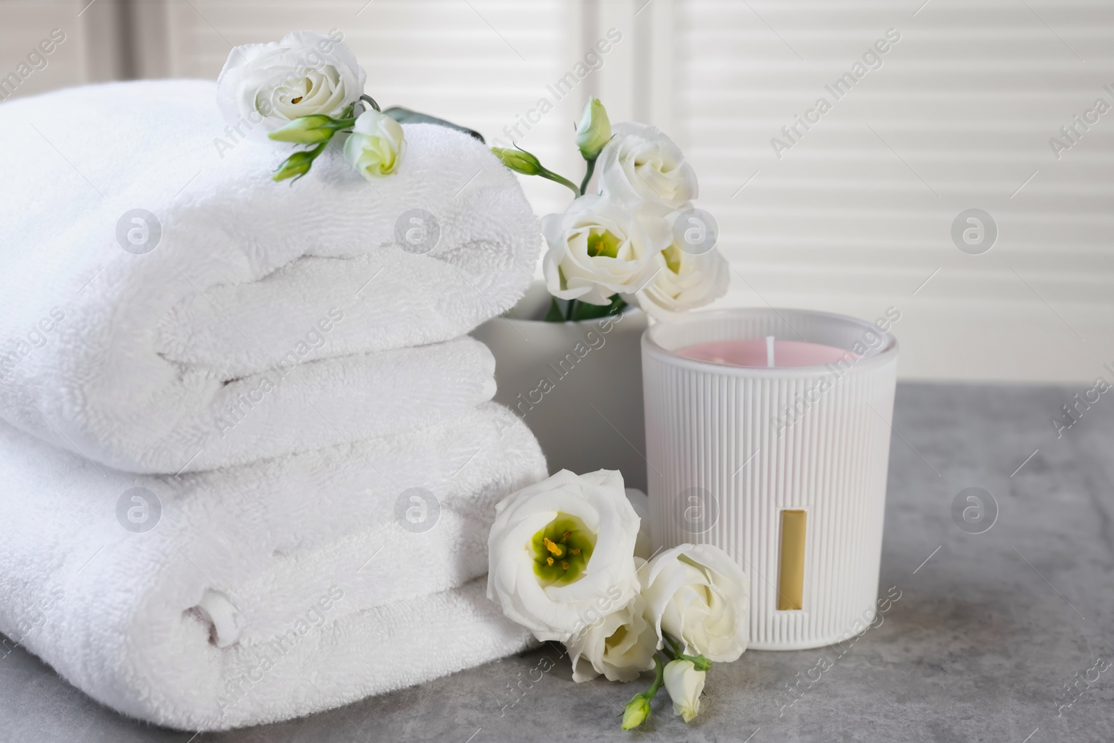 Photo of Scented candle, folded towels and eustoma flowers on gray marble table