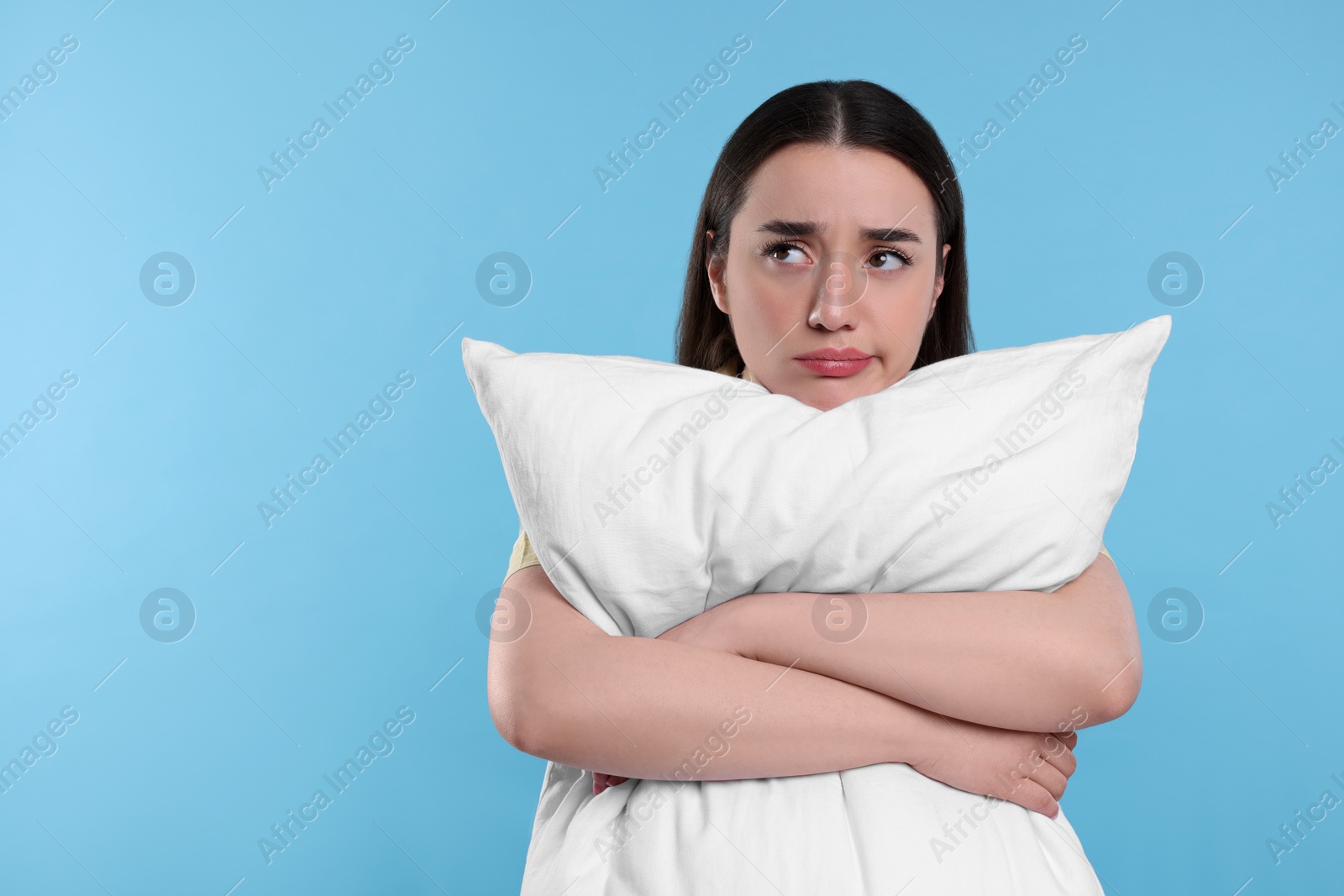 Photo of Tired young woman with pillow on light blue background, space for text. Insomnia problem