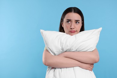 Tired young woman with pillow on light blue background, space for text. Insomnia problem