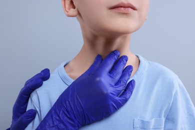 Endocrinologist examining boy's thyroid gland on light grey background, closeup