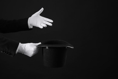Magician holding top hat on black background, closeup. Space for text