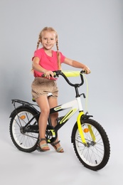 Photo of Cute little girl riding bicycle on grey background