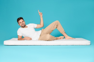 Photo of Man on soft mattress pointing upwards against light blue background