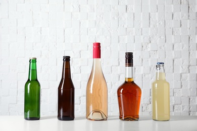 Bottles with different alcoholic drinks on table near white wall