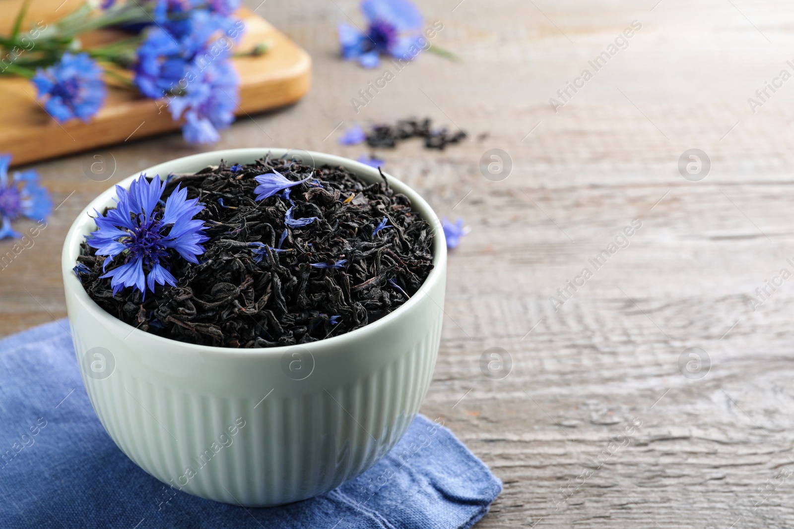 Photo of Bowl with dry tea leaves and cornflower on wooden table. Space for text