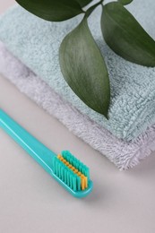 Photo of Plastic toothbrush, towels and green leaves on light background, closeup