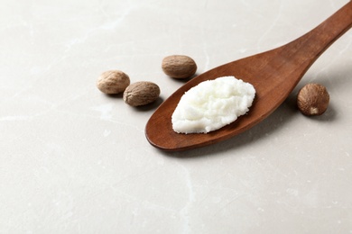 Shea butter in wooden spoon and nuts on table. Space for text