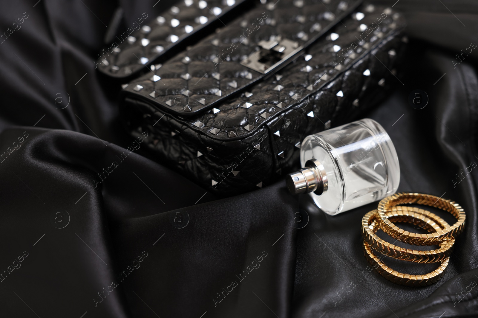 Photo of Leather bag, bottle of perfume and golden bracelets on black fabric, closeup. Space for text