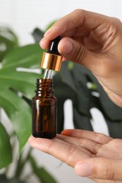 Woman with bottle of cosmetic serum near green plant, closeup