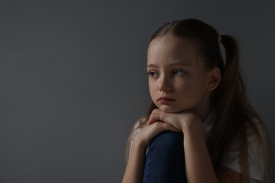 Sad girl sitting near dark grey background, space for text